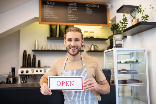 Satisfied man near counter in cafe inviting visitors - Photo, Image