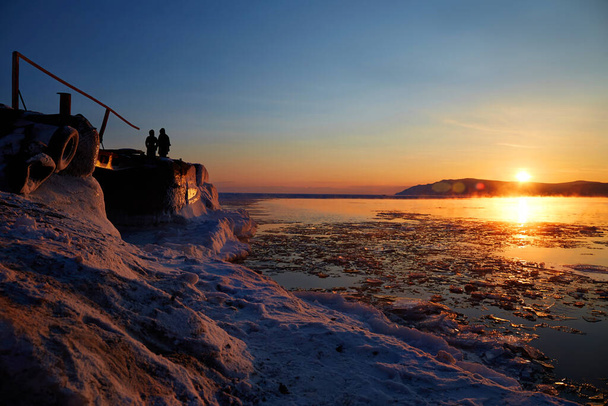 Schöner Sonnenuntergang am Baikalsee. Auf der Seebrücke beobachten ein Mann und eine Frau den Sonnenuntergang. Schmelzendes Eis im See. - Foto, Bild