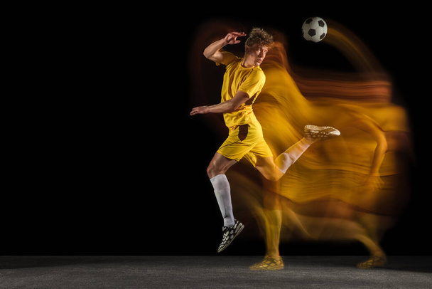 Young caucasian male football or soccer player kicking ball for the goal in mixed light on dark background. Concept of healthy lifestyle, professional sport, hobby. - Fotó, kép