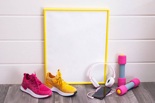 sports at home - dumbbells and multicolored sneakers, a sign, with a yellow frame, for notes, headphones and a cell phone on a white background - Photo, Image