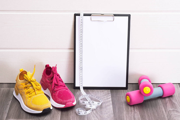 sport at home - pink and yellow sneakers, dumbbells and a note board and measurement tape close-up - Fotografie, Obrázek