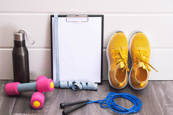 sports equipment - yellow sneakers, dumbbells, jump rope and plate, measurement tape and black water bottle, close-up - Foto, Imagem