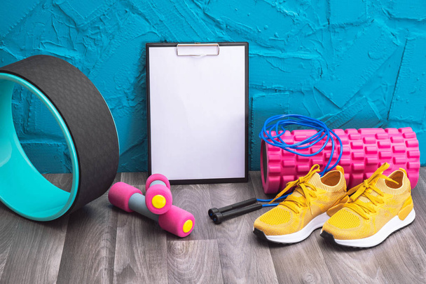 workout at home - yellow sneakers, dumbbells, jump rope, measurement tape, note plate and massage roller, close-up and blue background - Foto, Bild