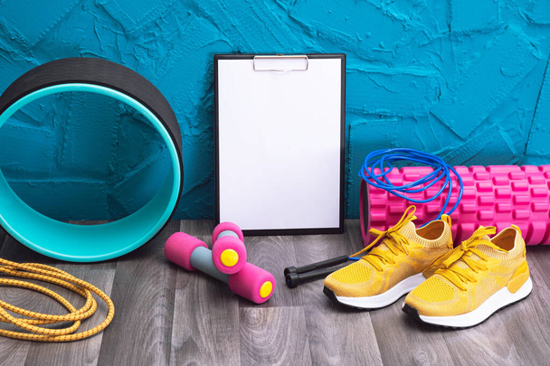 yellow sneakers, dumbbells, skipping rope, measurement tape, note board and massage rollers, close-up and blue background - Φωτογραφία, εικόνα
