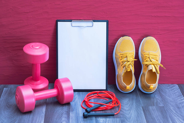 workouts at home - red dumbbells, jump rope and yellow sneakers, note board, close-up and red background - Fotó, kép