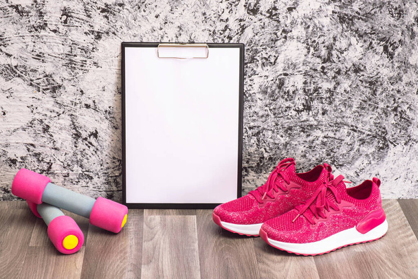 plate of notes, pink sneakers and dumbbells for workout at home, on a textured background - Photo, image