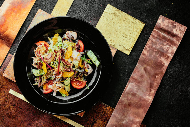 salad with ham, orange slices, tomato, cucumber and lettuce leaves in a black plate on a copper background. close up. top view - Fotoğraf, Görsel