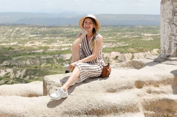 Lächelndes Mädchen auf Felsen sitzend, schöne Landschaft im Hintergrund, Kappadokien. - Foto, Bild