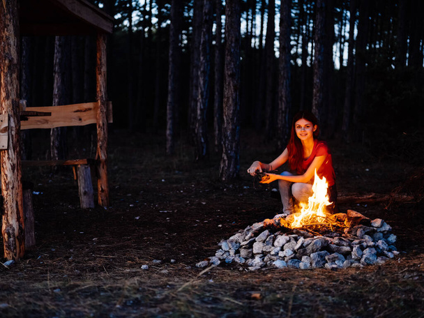 Akşamları çam ormanında kamp ateşinin yanında bir kadın. - Fotoğraf, Görsel