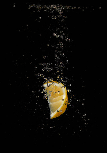 Lemon splashing in water on a black background - Фото, изображение