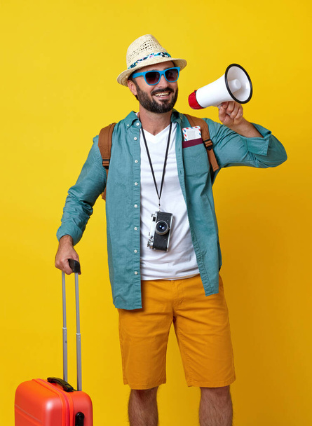 Sırt çantası, bavulu ve sarı arka planda fotoğraf makinesi olan neşeli bir adam. - Fotoğraf, Görsel