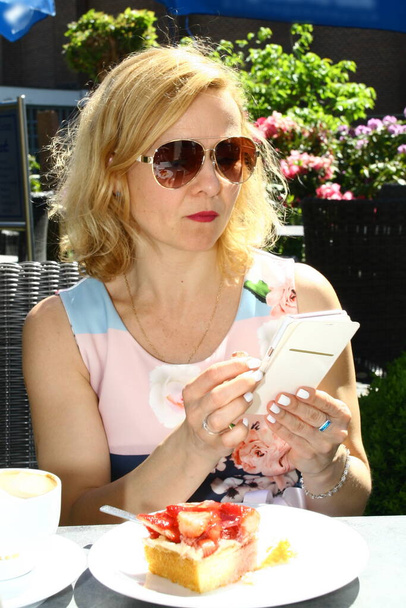 γυναίκα με γυαλιά ηλίου σε μια καφετέρια, ανάγνωση κάρτα μενού - Φωτογραφία, εικόνα