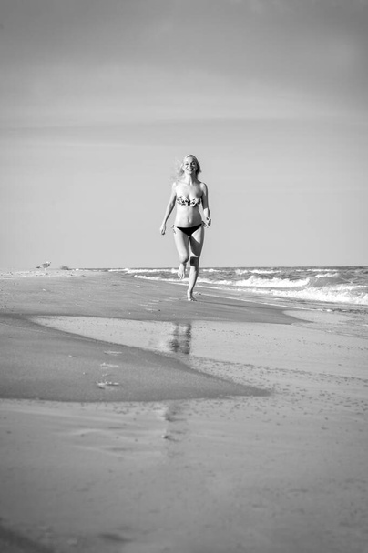Beautiful sexy blonde girl in a swimsuit runs in the surf on a sandy beach - Fotoğraf, Görsel