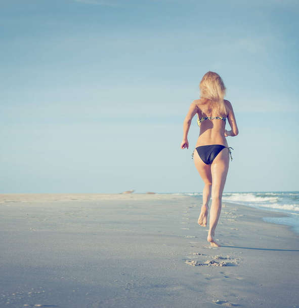 Beautiful sexy blonde girl in a swimsuit runs in the surf on a sandy beach - Foto, afbeelding
