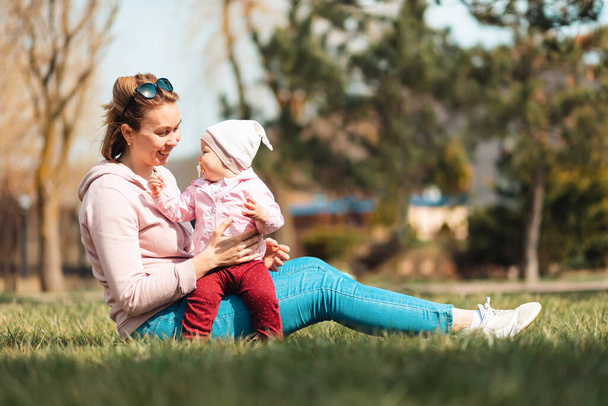 幸せな笑顔の母親は彼女の子供を抱きかかえて、草の上に座っています。子供と家族の屋外レクリエーション. - 写真・画像