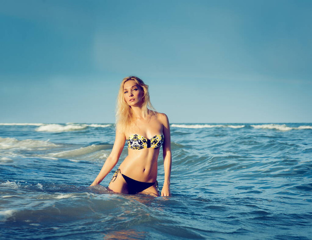 Beautiful sexy blond girl in a swimsuit posing on a sandy sea beach near the water - Foto, afbeelding