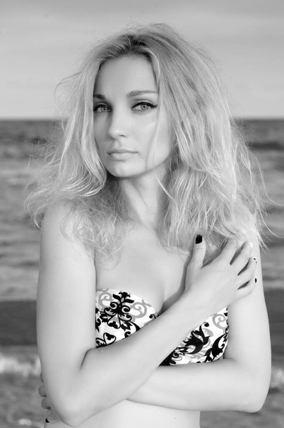 Beautiful sexy blond girl in a swimsuit posing on a sandy sea beach near the water - Foto, Imagen