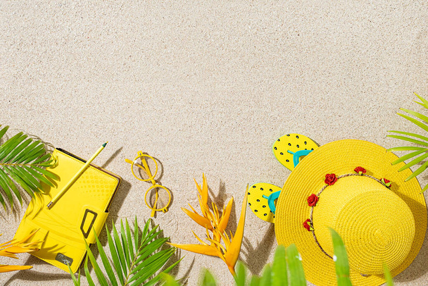 Vista superior del sombrero redondo amarillo, y hojas de palma en la playa de arena - Foto, Imagen