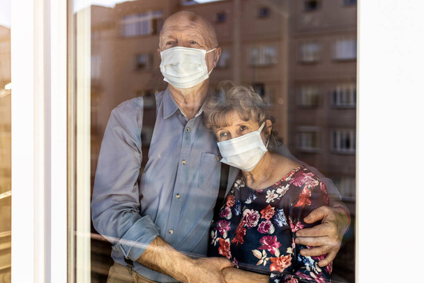Bezorgd stel dat thuis door het raam kijkt tijdens de COVID-19 epidemie - Foto, afbeelding