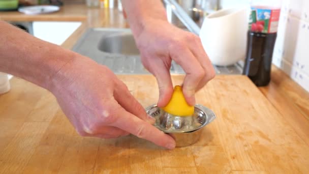Espremendo o suco de um cintron murchado em um espremedor de aço inoxidável, preparando a bebida. Mesa de madeira na cozinha - Filmagem, Vídeo