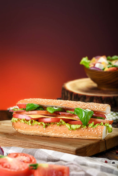 Baguette sandwiches with Ham, sliced cheese, tomatoes and fresh lettuce on wooden cutting board. Dark red background.  - Valokuva, kuva