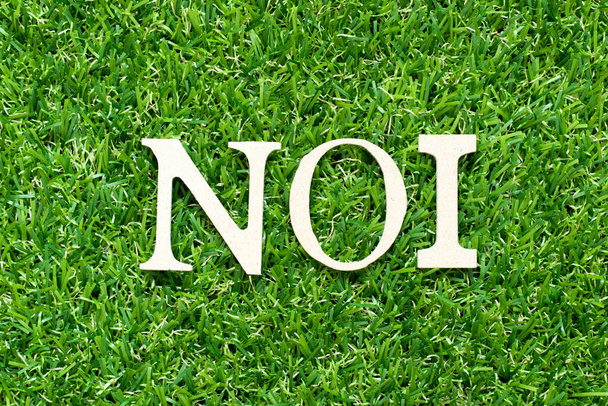 Літера Alphabet в слові NOI (абревіатура Net операційного доходу або не індексована) на зеленому тлі трави - Фото, зображення