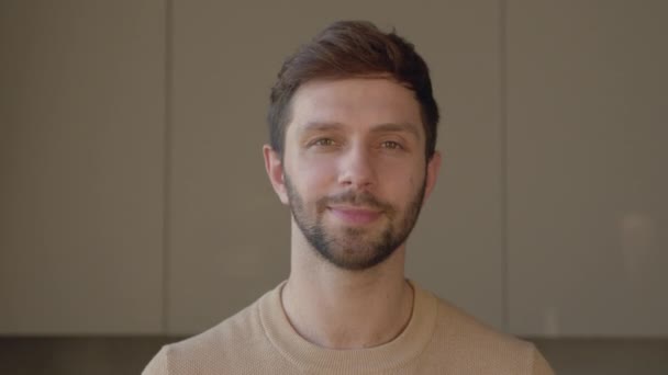 Portret van een jonge glimlachende man die naar de camera kijkt, slow motion concept. Jonge professionele man op zoek naar camera thuis - Video