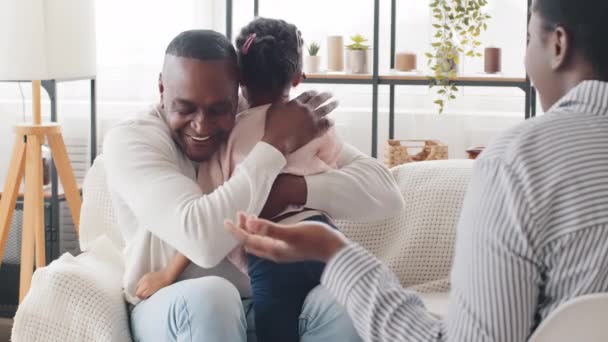 Mature man african father holding little daughter child girl talking to unrecognizable unknown afro woman sitting indoor, black caring dad hugging cuddling baby kid calms sad upset schoolgirl consoles - Footage, Video