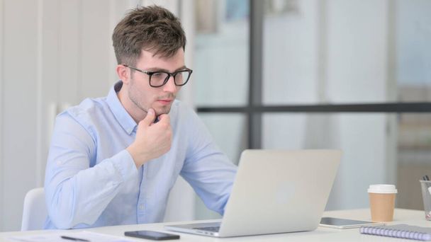 Fiatal férfi laptop gondolkodás a munkahelyen  - Fotó, kép