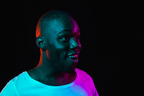 Young happy African-American man isolated on dark background in neon light - Foto, imagen