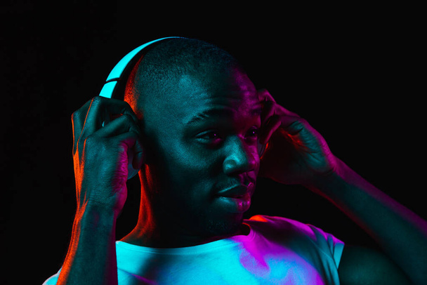 Young African-American man isolated on dark background in neon light - Foto, imagen