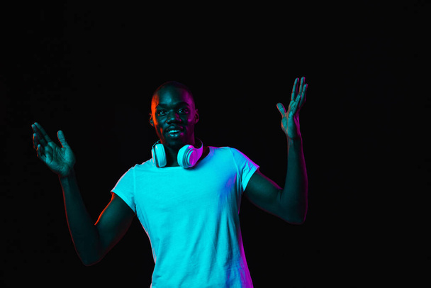 Portrait of young African man isolated on dark background in neon light - Foto, imagen