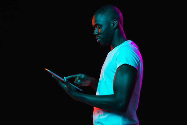 Young African-American man isolated on dark background in neon light - Photo, Image