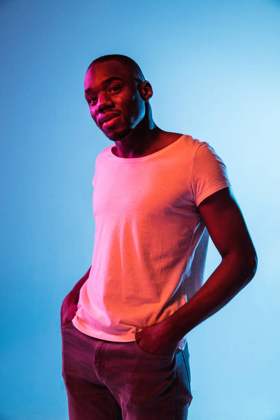 Jovem modelo de moda masculina posando isolado no fundo azul em luz de néon - Foto, Imagem
