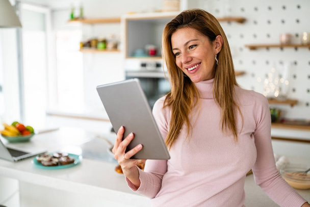 Beautiful woman in kitchen looking at recipe on tablet - Foto, immagini