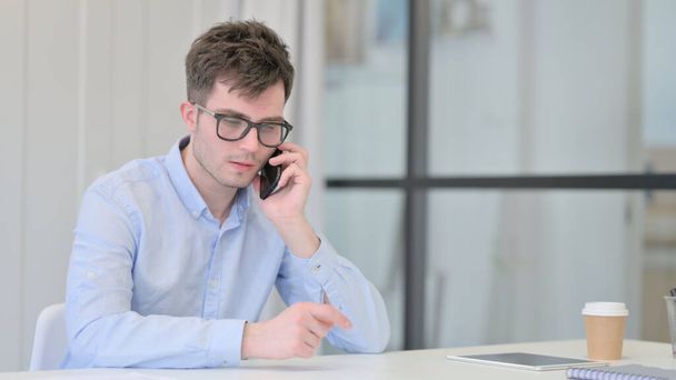 若い男はオフィスで電話で話している  - 写真・画像