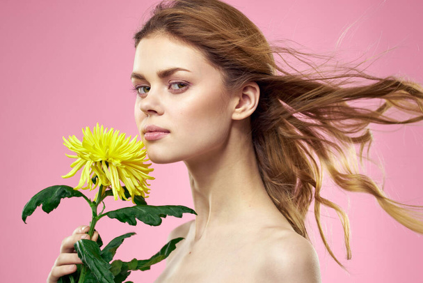 Krásná dívka se žlutou květinou na růžovém pozadí nahé ramena make-up - Fotografie, Obrázek