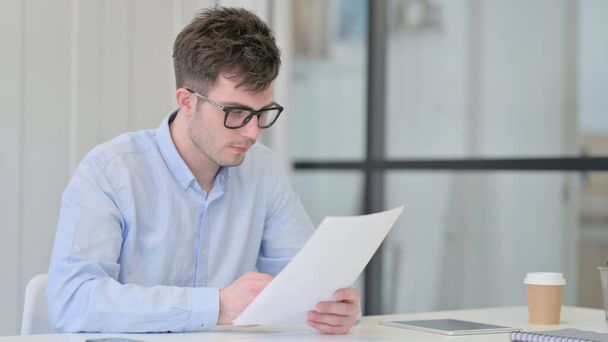 Ο νεαρός άνδρας διαβάζει έγγραφα στο γραφείο  - Φωτογραφία, εικόνα