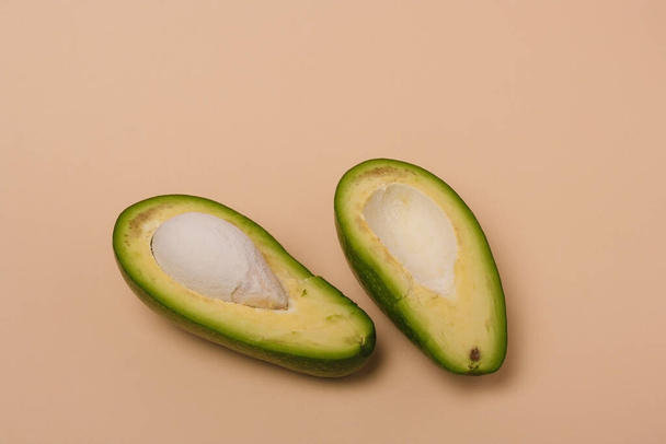 Дві половинки зеленого свіжого авокадо з насінням на бежевому фоні. Мінімальна стилізована композиція
. - Фото, зображення