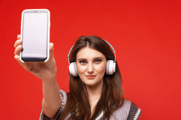 Μια νεαρή γυναίκα ακούει μουσική με ακουστικά στο κινητό της. - Φωτογραφία, εικόνα