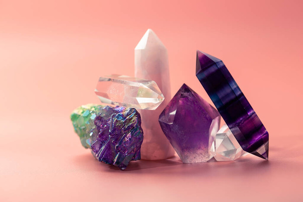 Различные граненые кристаллы для исцеления и магической практики. Куча красивых полудрагоценных камней. Аметист, розовый кварц, флюорит, горный кристалл на пастельно-розовом фоне - Фото, изображение