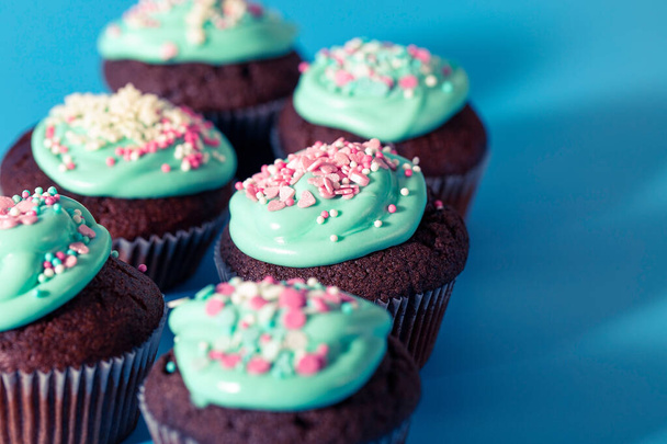 Chocolate cupcakes decorated with icing sugar and sprinkles at home. Festive sweet food close-up on a blue background - Photo, Image