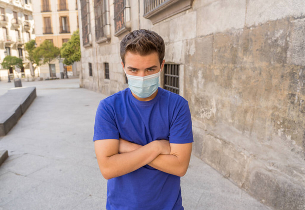 Young sad desperate man wearing surgical face mask in public spaces. Man with protective mask walking outdoors city street after coronavirus outbreak lockdown. New Normal life and COVID-19. - Photo, image