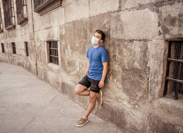 Young sad desperate man wearing surgical face mask in public spaces. Man with protective mask walking outdoors city street after coronavirus outbreak lockdown. New Normal life and COVID-19. - Photo, Image