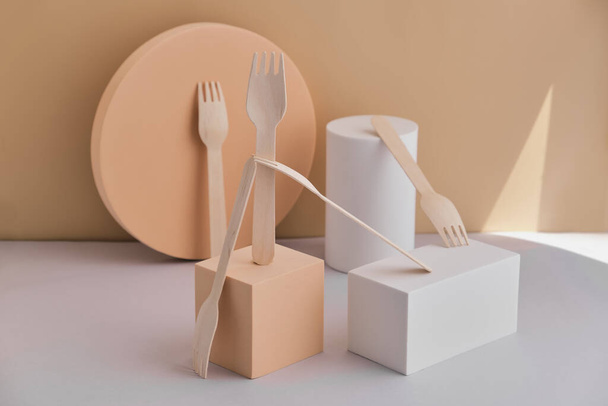 Set van milieuvriendelijk servies, houten vorken geplaatst op trendy podia en geometrische sokkels, minimalistische abstracte compositie op een licht beige ondergrond. - Foto, afbeelding