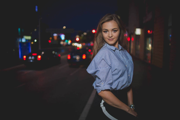 A shallow focus of a young Caucasian woman with long hair posing on the street at night - 写真・画像