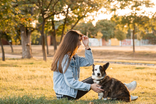 joven hembra abrazando su galés corgi perro en primavera park - Foto, Imagen