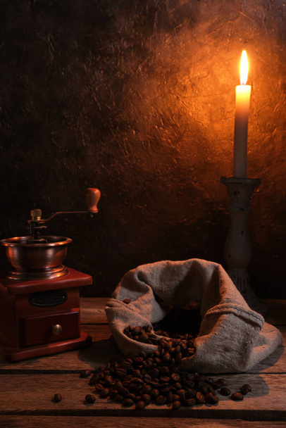 Coffee beans are scattered from bag on an old wooden table, with candle burning in background - Φωτογραφία, εικόνα