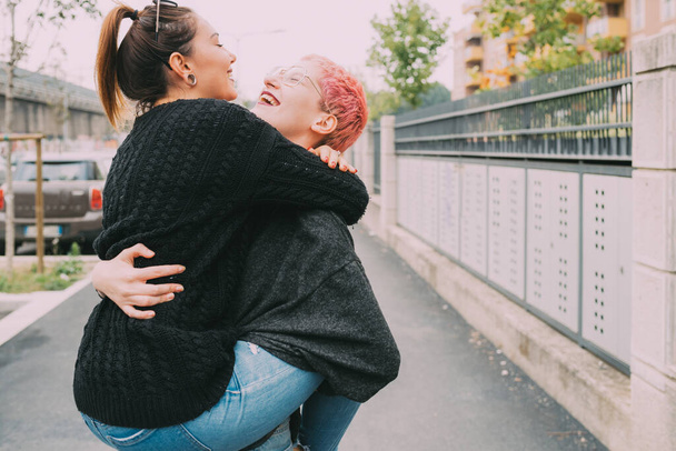 Two happy young women friends outdoor city hugging laughing celebrating good times together - Photo, Image