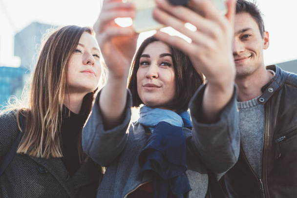 three people outdoor holding smart phone taking selfie - Photo, Image